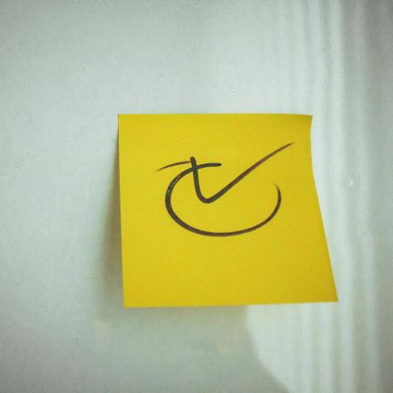 Yellow sticky note with a check mark symbol on a white background, ideal for reminders.