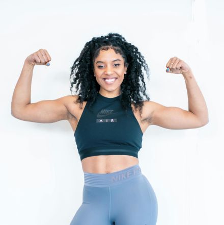 Strong woman posing indoors, showcasing fitness and strength with a confident smile.